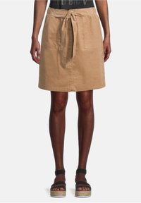 Kaki kjol med midjeband, med två framfickor och rak skärning. Materialet verkar strukturerat och hållbart. Platta, plattformssandaler.