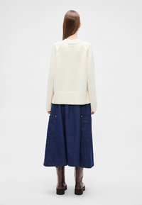 Κρεμ πλεκτό πουλόβερ με ριμπ τελείωμα, συνδυασμένο με μακρύ μπλε τζιν φούστα με μεγάλες τσέπες και καφέ μπότες μέχρι το γόνατο.