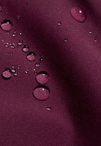 Wasserabweisender kastanienbrauner Stoff mit glatter Textur, der verstreute Wassertropfen zeigt, die das Licht auf der Oberfläche reflektieren.