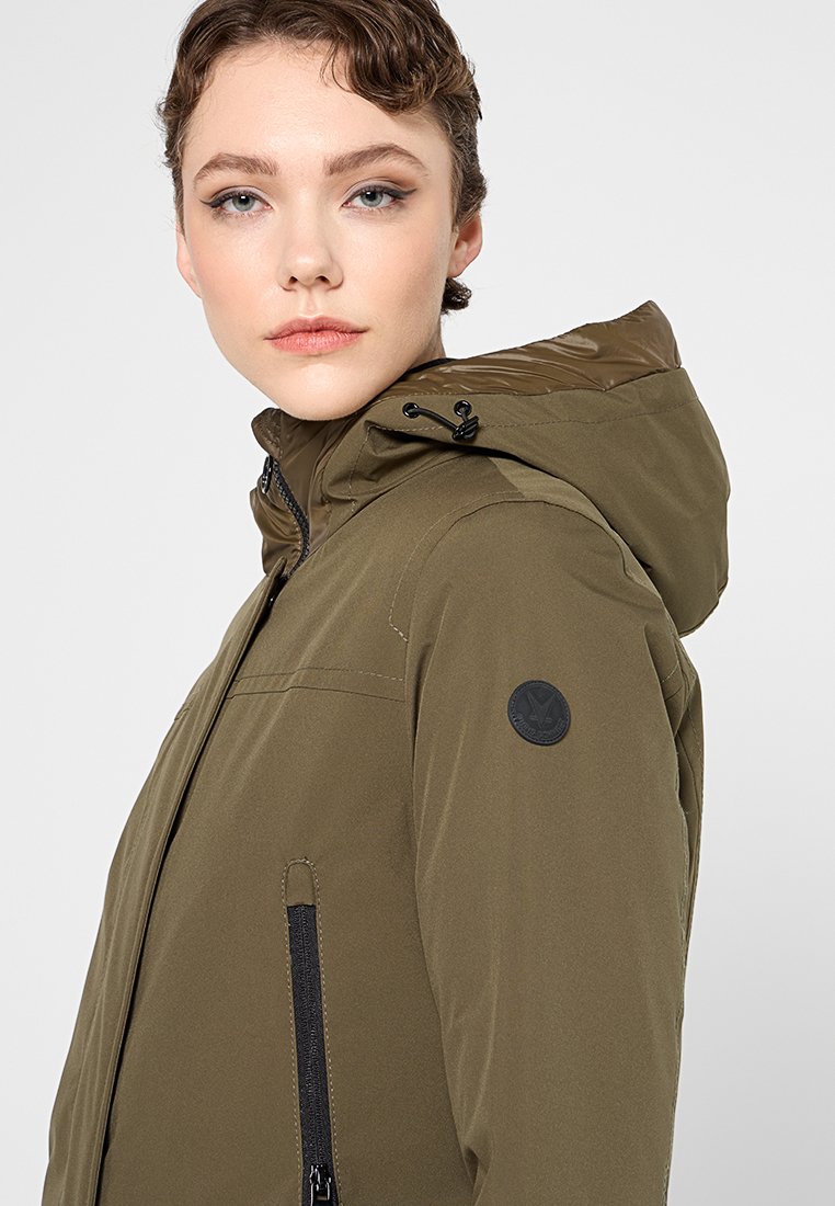 Veste à capuche vert olive en matériau imperméable avec une fermeture éclair sur le devant, des poches latérales et un patch circulaire sur l'épaule gauche.