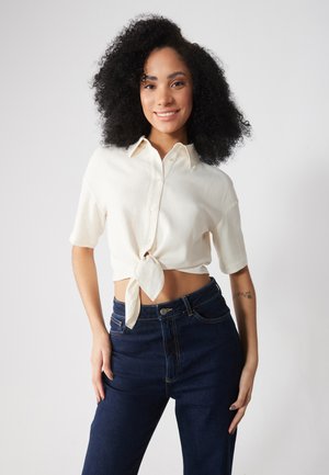 Crème korte mouwen blouse met strik en een kraag, gecombineerd met hoge taille donkere spijkerbroek met knoopsluiting en zakken.