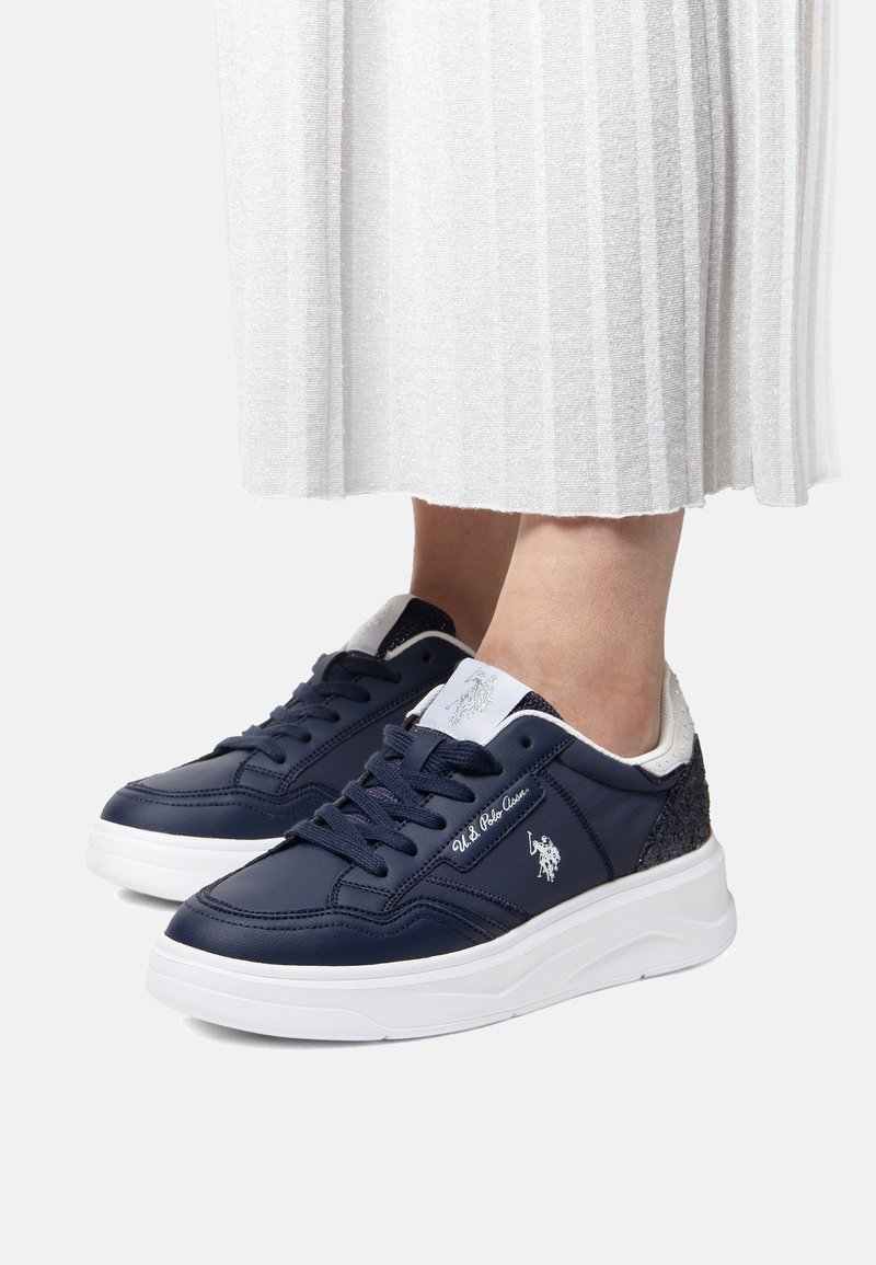 Navy blue sneakers with leather upper, white sole, and silver accents. Features logo, lace-up design, and textured heel detail.