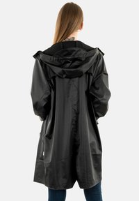 Cappotto impermeabile nero, design oversize, tessuto testurizzato, cappuccio regolabile e tasche laterali. La vista posteriore mette in evidenza l'orlo arrotondato.