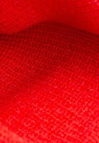 Roter strukturierten Stoff, dicht gestrickt mit einer glatten Oberfläche, die ein einheitliches Muster aus kleinen eingewebten Schlaufen zeigt.