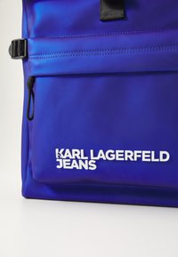Modra najlonska torba z gladko teksturo, z belim logotipom "KARL LAGERFELD JEANS" in črnim prilagodljivim trakom.