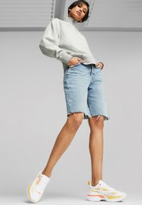 Sweatshirt gris à col haut, short en jean bleu clair usé, et baskets blanches avec accents orange et jaune. Coupe slim, look décontracté.