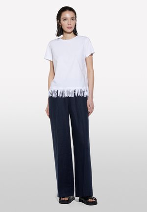 T-shirt en coton blanc avec un ourlet à franges, associé à un pantalon bleu marine ample et des sandales noires. Design simple et décontracté avec des détails minimaux.