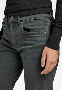 Vaqueros G-Star grises, fabricados en denim, con un ajuste slim, diseño de cinco bolsillos y una etiqueta negra en la cintura. Textura suave y sin patrones visibles.