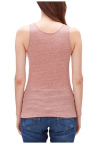 Mujer con una camiseta sin mangas de color rosa polvo y jeans azules, vista desde atrás sobre un fondo blanco.