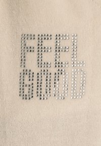 Beige Stoff mit strukturiertem Finish, verziert mit silberfarbenen Strasssteinen, die "FEEL GOOD" in Blockbuchstaben buchstabieren.