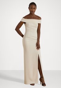 Off-the-shoulder smėlio spalvos vakarinių suknelė su prigludusia siluetu ir šlaunų aukščio plyšiu. Lygi medžiaga ir elegantiškas siluetas.