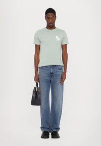 Lys grønn bomulls t-skjorte med trykt logo, kombinert med blå rette denimjeans og en svart veske, fullført med svarte sko.