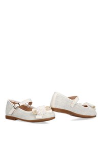 Zapatos Mary Jane de color crema con un acabado texturizado, que presentan un acento de flor, cierres con tira y una suela de goma marrón.
