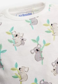 Balta kokvilnas auduma, kas rotāta ar atkārtotu pelēku koalas un mīksto zaļo lapu rakstu. Apkaklei ir ribota apdare un kniedēšanas aizdare.