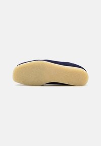 Sapata de tecido azul-marinho com uma parte superior suave e texturizada e sola de borracha amarela flexível, apresentando um design de bico liso e arredondado.