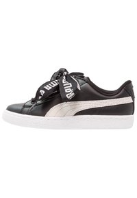 Černé kožené tenisky s krémovým pruhem a texturovanou bílou gumovou podrážkou. Mají velké černé a bílé šněrování. Nízkoprofilový design.