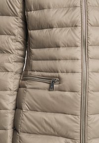 Beige pufferväst med quiltad textur, utrustad med en silverfärgad dragkedja och en dragkedjeförsedd ficka på vänster sida. Slätt, vattenavvisande material.