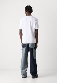 White cotton t-shirt paired with wide-leg jeans featuring a patchwork of light and dark denim. The jeans have side pockets and a relaxed fit.