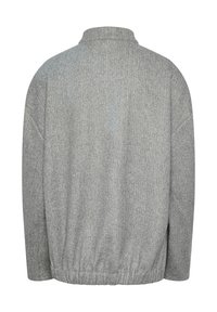 Grå ulljacka med hög krage, löst snitt och elastisk nederkant. Har texturerad tyg och design med sänkt axel för komfort.