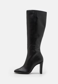 Botte noire en cuir montant jusqu'au genou, avec un bout pointu, un talon stiletto fin et une texture lisse. Design minimaliste sans éléments métalliques visibles ni motifs.