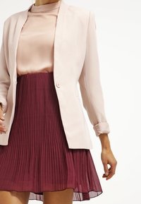 Różowa marynarka o dopasowanym kroju, zestawiona z bordową spódnicą w plisy. Spódnica ma swobodną fakturę i subtelny połysk.