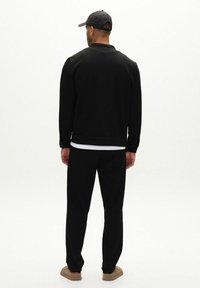 Svart sweatshirt med rund hals och långa ärmar, kombinerad med matchande svarta byxor. Outfitten har en avslappnad passform och mjuk tygtextur.