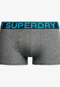 Boxers grises con un acabado texturizado y una cinturilla sólida de color oscuro que presenta la palabra "SUPERDRY" en letras turquesa brillantes.