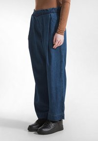 Blauwe denim wijde broek met een elastische tailleband en zijplooien. Gepaard met zwarte sneakers.