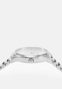 Sølvfarget klokke med rund kasse, teksturert hvit skive, og metallarmbånd med en lenkedesign. Inkluderer detaljert krone.