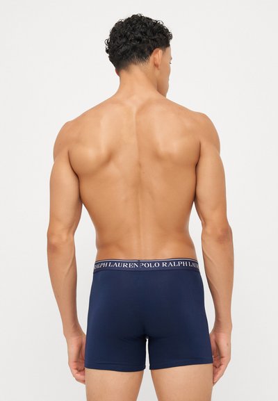 Boxers de cor azul-marinho com um tecido sólido e uma cinta contrastante, apresentando o logótipo "Polo Ralph Lauren" em branco. Textura suave.