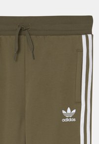 Olivgröna sweatpants med dragsko i midjan, vita sidostrikar och en liten vit Adidas-logotyp på framfickan. Mjuk tygtextur.