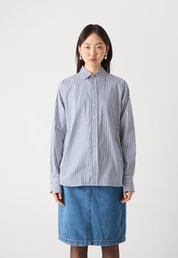 Randig skjorta i blått och vitt, med långa ärmar, krage och bröstficka, i kombination med en denimkjol som går till knäna.