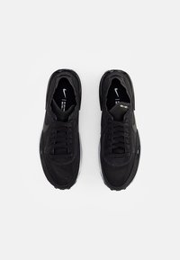 Tênis pretos com parte superior em tecido, fecho de cadarço e colarinho acolchoado. Apresentando uma entressola branca e uma discreta marcação preta nas laterais.