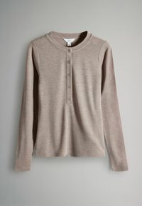 Kerge beeži värvi pikka varrukatega henley särk viie nupuga, ümmargune kaelus ja pehme, kergelt tekstureeritud kangas, mis ripub halli tausta ees.