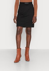 Svart knälång kjol med rak skärning, tillsammans med ett smalt svart bälte. Ett par bruna läderstövlar vid ankeln med en modest klack.