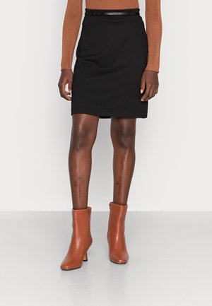 Jupe noire droite arrivant au genou, accompagnée d'une ceinture noire étroite. Une paire de bottines en cuir marron avec un talon modeste.
