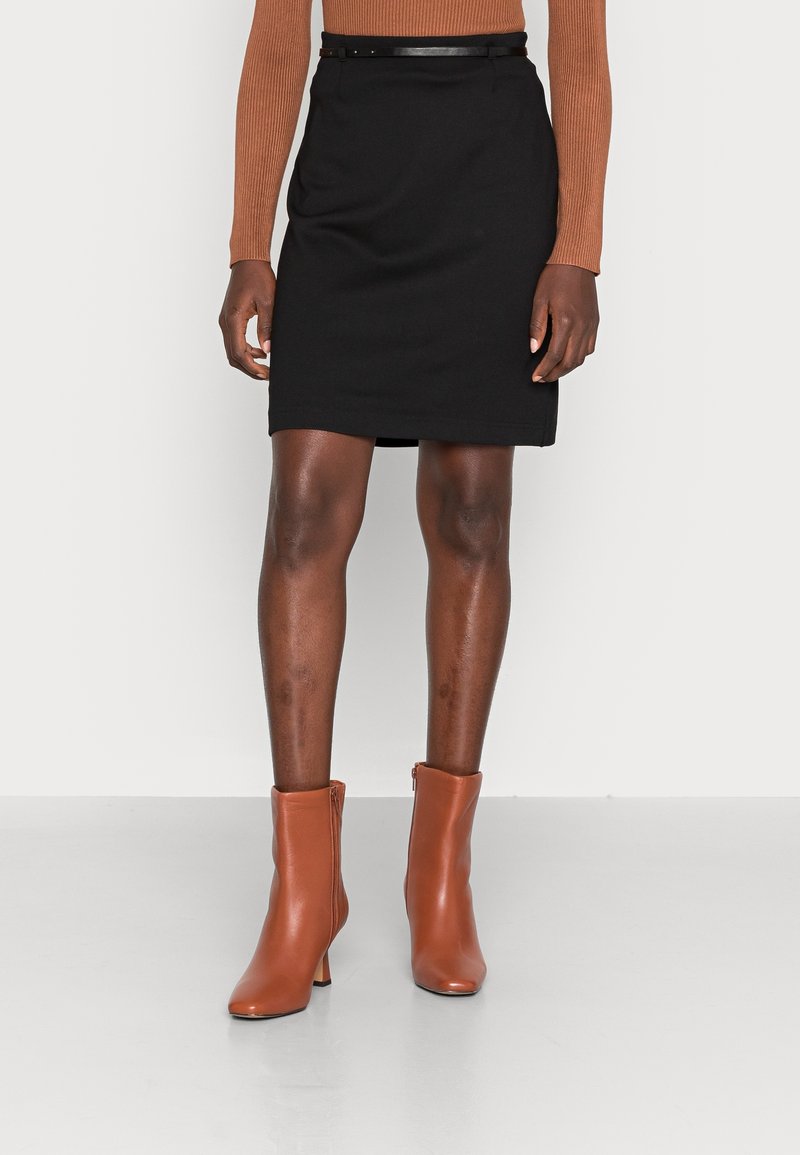 Svart knälång kjol med rak skärning, tillsammans med ett smalt svart bälte. Ett par bruna läderstövlar vid ankeln med en modest klack.