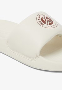 White slide sandal made of smooth synthetic material, featuring a wide strap with a circular red logo and textured footbed for comfort.