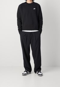 Černá mikina s malým bílým logem Nike, doplněná volnými černými kalhotami s jemným pruhovaným vzorem a černobílými teniskami.