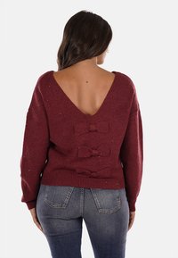 Maglione borgogna lavorato a maglia con scollo a V profondo, con tre fiocchi di tessuto e sottili accenti glitterati. Tessuto leggermente strutturato.