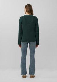 Grüner, strukturierten Strickpullover mit Rundhalsausschnitt, langen Ärmeln und lockerer Passform, kombiniert mit hellblauen, ausgestellten Jeans und beigen Schuhen.