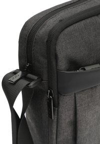 Borsa in tessuto grigio scuro con un design snello, dotata di cerniere nere, tracolla regolabile e dettagli in plastica per una maggiore durata.
