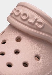 Κοντινό πλάνο ενός ροζ παπουτσιού Crocs που δείχνει την υφή της επιφάνειας, τις οπές αερισμού και το ανάγλυφο λουράκι με το όνομα της μάρκας.