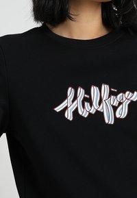 Czarna bluza z kolorowym logo "Hilfiger" w falistym kroju liter, z jasnoniebieskimi i czerwonymi akcentami na gładkiej, bawełnianej tkaninie.