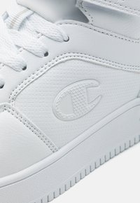 Sneaker alb din piele, cu accente texturate, vârf rotund și talpă din cauciuc alb. Include un logo hexagonal pe lateral. Șireturile sunt albe.