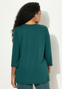 Teal, pitkähihaine paita, jossa on pyöreä kaula-aukko ja rento malli. Pehmeä, sileä kangas, jossa on hieman kaareva helma ja ei näkyviä kuvioita.