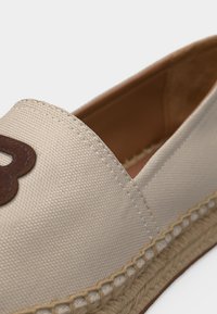 Μπεζ εσπαντρίγια από καμβά με πλεκτή σόλα από γιούτα και διακοσμητικό καφέ δερμάτινο γράμμα στο πάνω μέρος.