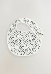 Bavoir blanc avec un motif à pois noirs, en forme courbée, et une sangle ajustable dotée de deux fermetures à pression pour un maintien sécurisé.
