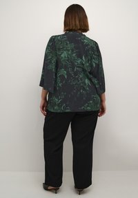 Blusa floreale verde scuro con maniche a tre quarti, abbinata a pantaloni neri a gamba larga e tacchi neri. Tessuto dalla superficie liscia.