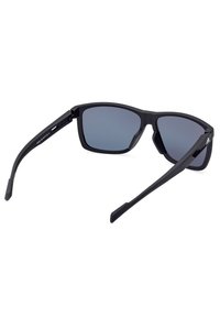 Mustat aurinkolasit, joissa on matta pinta, suorakulmainen kehys ja harmaan sävytetty linssi. Vankat varret on varustettu kevyellä kaarevuudella mukavuutta varten.